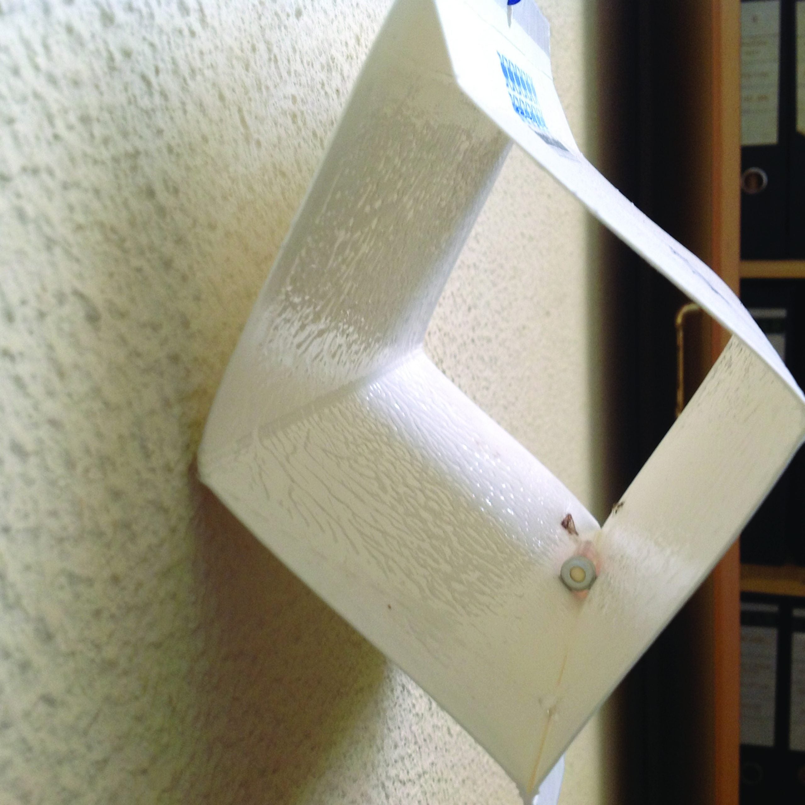 Sticky insect monitoring trap mounted on a wall to detect and capture indoor crawling pests like cockroaches or ants in office or residential spaces.