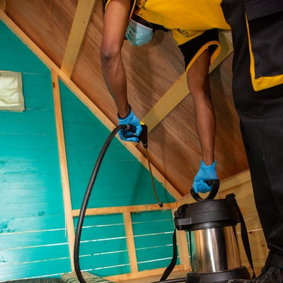 Schtäger pest control technician using a vacuum system to treat a wooden cabin interior for bed bugs and indoor pests.
