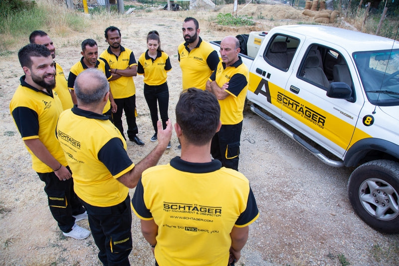 Schtäger pest control team in yellow uniforms having a meeting next to a branded service truck in an outdoor work site.