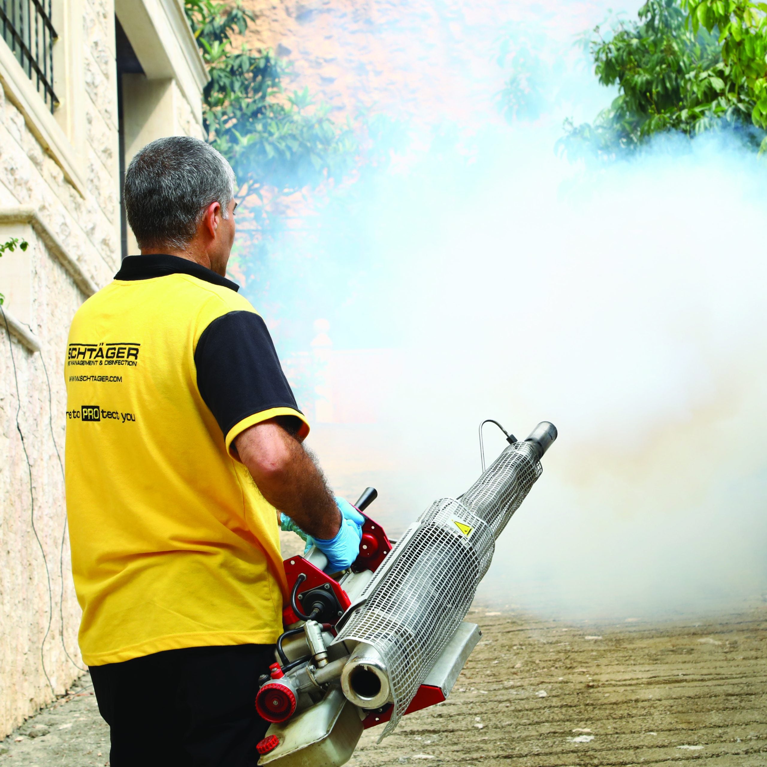 Schtager Pest Control technician using a thermal fogging machine for outdoor mosquito control and disinfection in a residential area.