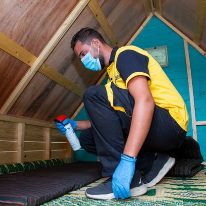Schtäger pest control technician spraying insecticide inside a wooden cabin to treat bed bugs and hidden pests in sleeping areas.